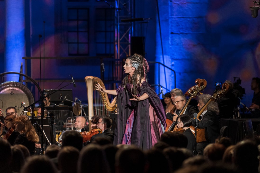 Śpiewająca Panna w długiej fioletowej sukni, w tle orkiestra.