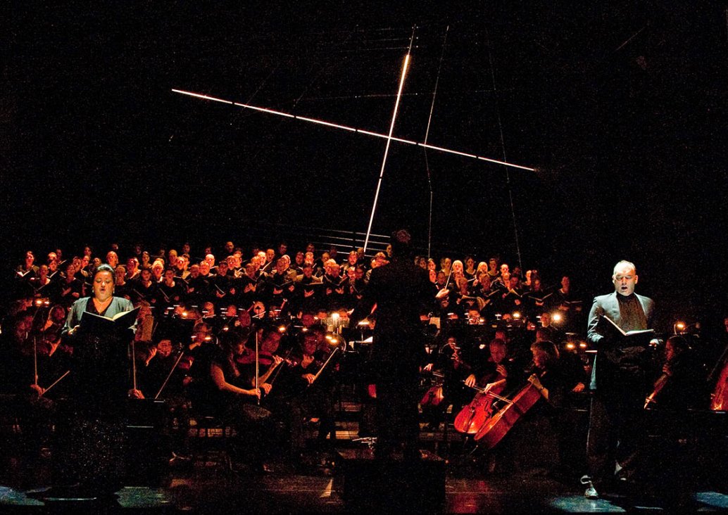 In the foreground there are four soloists and a conductor, all dressed up in concert clothes, soloists facing the audience, holding the notes in their hands, the conductor with his back to the audience - facing the performers. In the background, an orches