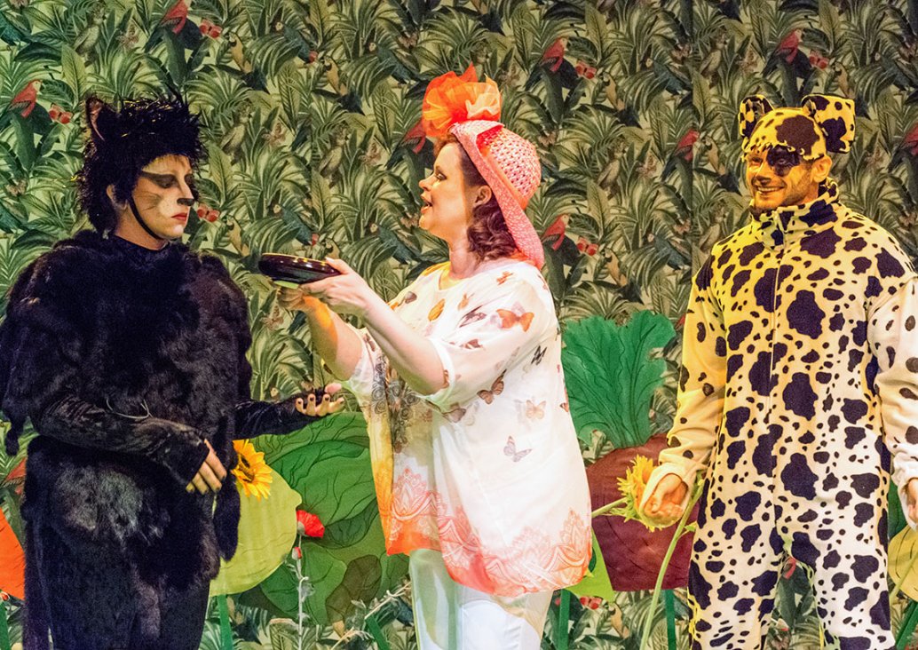 A group scene. On the left an actress dressed as a black cat, in the middle an actress in an airy butterfly-like blouse, addressing the cat, on the right a smiling actress dressed as a white dog in black patches.