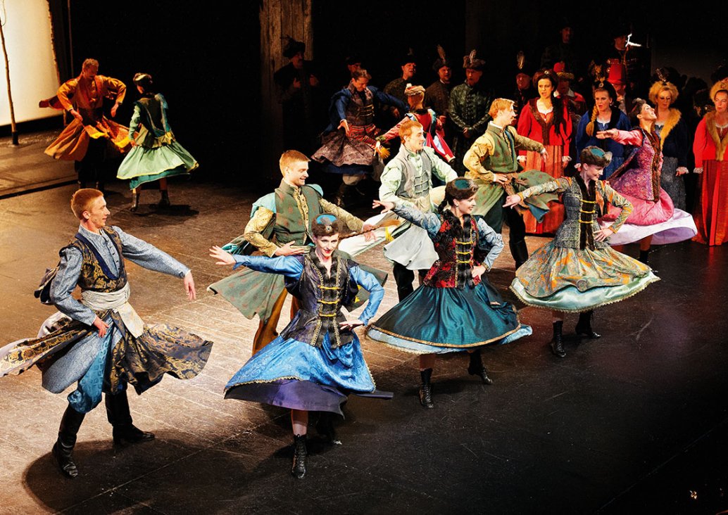 Grupa osób w kolorowych kontuszach tańczy mazura.