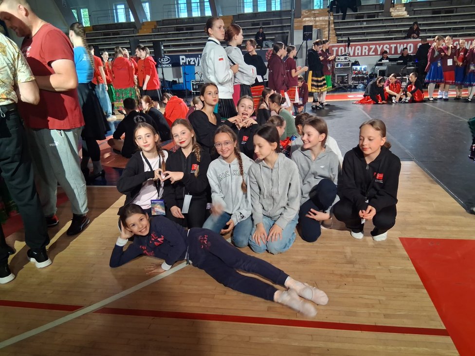 Grupa dziewczynek ubrana w dresy do ćwiczeń pozuje do zdjęcia w hali sportowej.