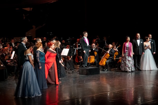Soliści Opery w wieczorowych strojach stoją na scenie, gotowi do ukłonu. W tle dyrygent Tomasz Tokarczyk i orkiestra.