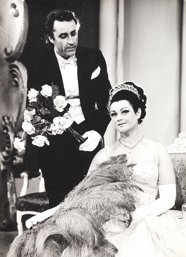 Czarno-biała fotografia przedstawiająca siedzącą Barbarę Barską-Féherpataky w eleganckiej sukni - kostiumie ze spektaklu "Hrabina Marica". Artystka trzyma w ręku wachlarz ze strusich piór. Po lewej stoi solista Jan Lachowski we fraku i z bukietem kwiatów,